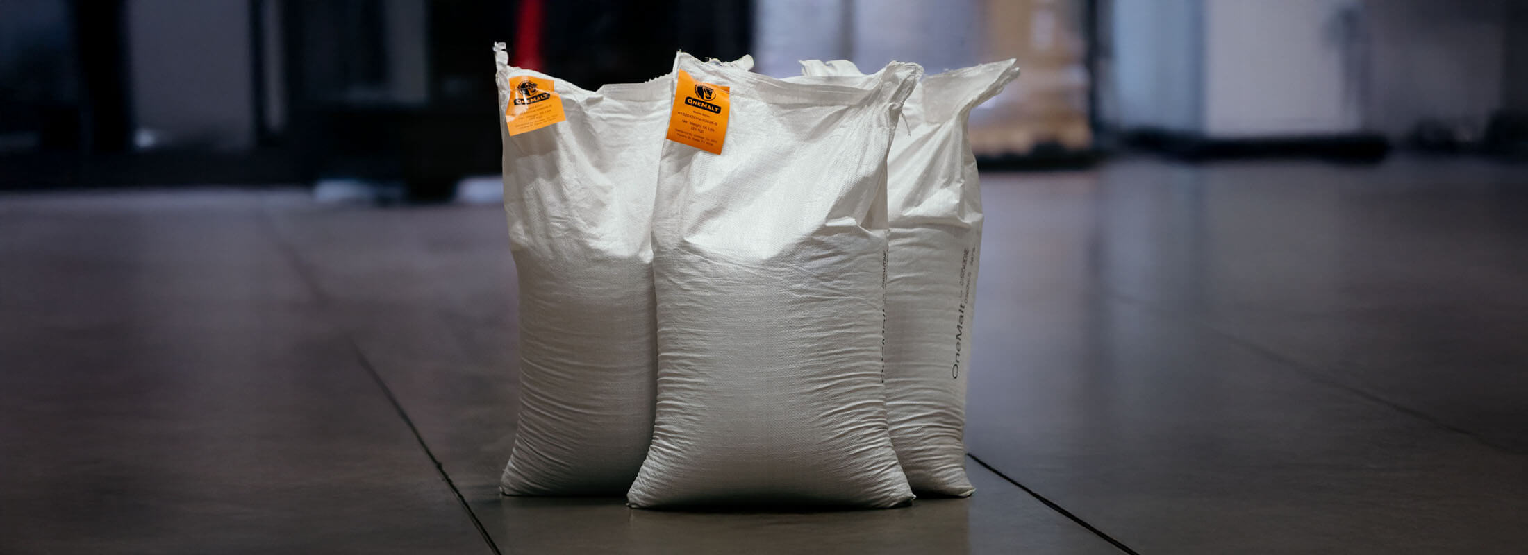 Three large white bags of malt on a warehouse floor