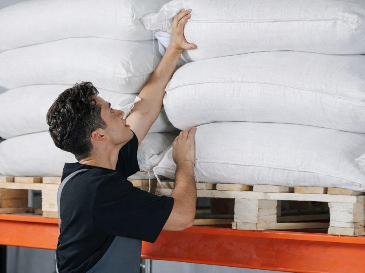 Man adjusting a stack of white bags on a pallet
